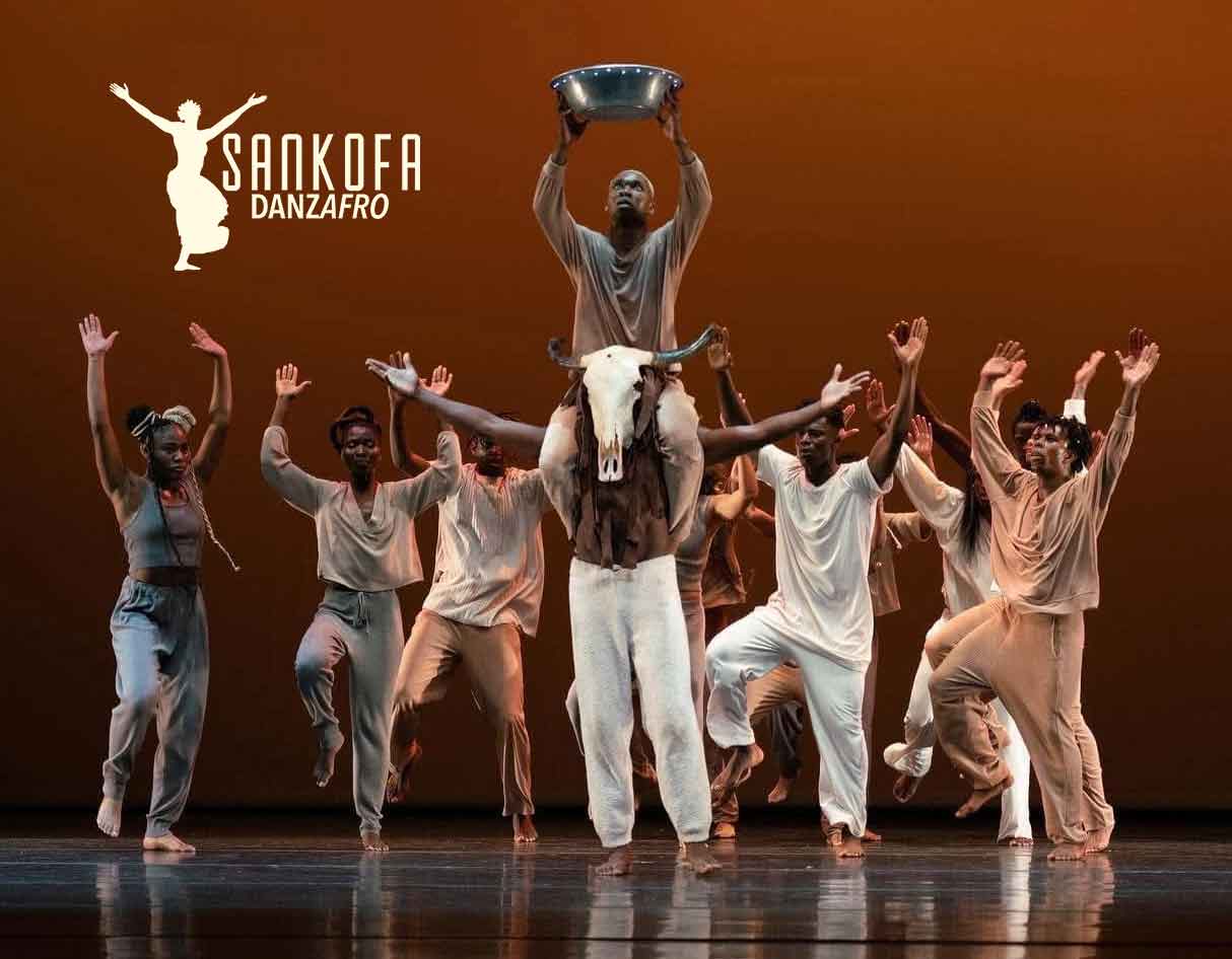 Afro-dance performance with a dancer lifted on others' shoulders, raising a metal bowl above head, onstage with Sankofa Danzafro logo in the top-left.